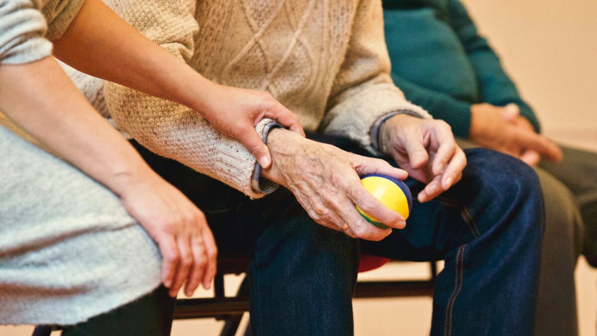 Le mani di un'operatrice accompagnano quelle di una persona anziana durante un esercizio riabilitativo