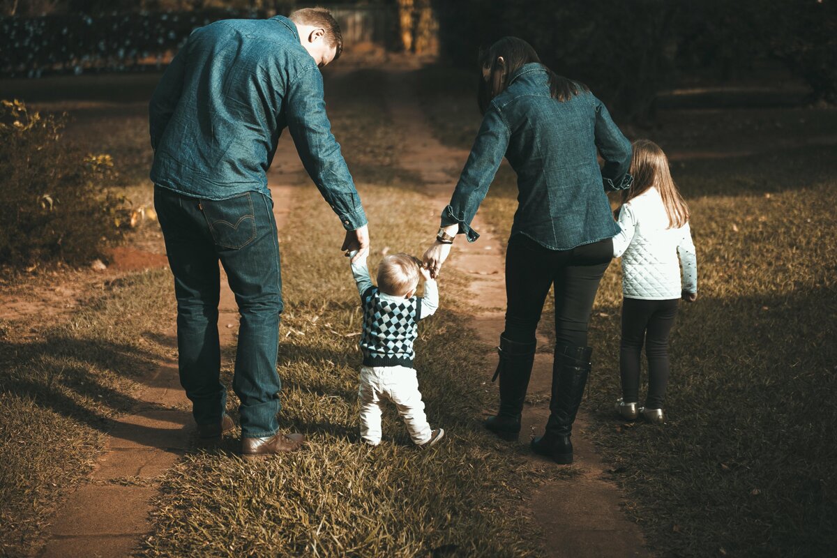 Una famiglia di quattro persone cammina di spalle su un sentiero tenendosi per mano